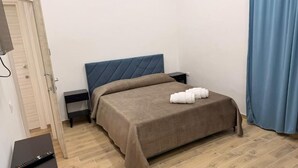 A bedroom with a bed, a nightstand, a remote control on a table, and a blue curtain.