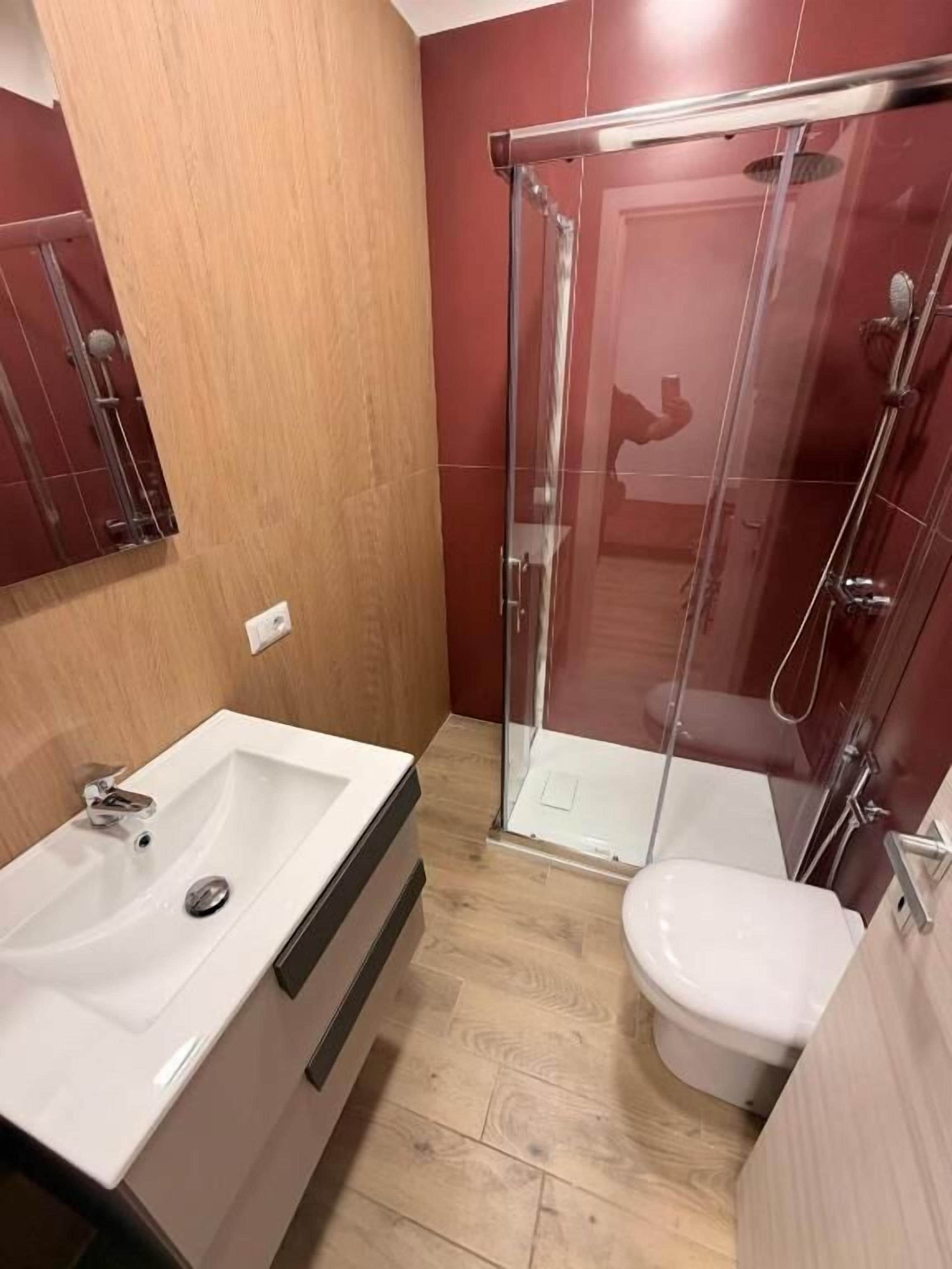 Un baño con ducha envuelta en vidrio, un lavamanos blanco y un inodoro.