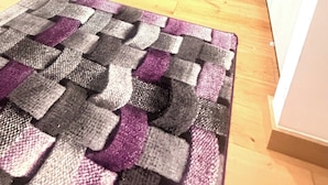 Een keuken met witte kasten, een inbouwoven en een magnetron. Er ligt een houten vloer en een kamerbreed tapijt met een patroon.