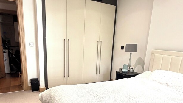 Een slaapkamer met een groot bed, een garderobe, een nachtkastje met een lamp, en een deur naar een badkamer.