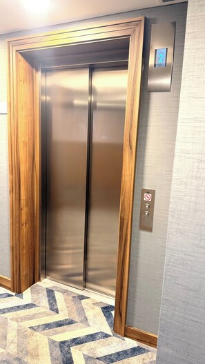 A hotel elevator with a wooden frame, a metallic interior, and a control panel with a number display. - Apartment Sleeps 6 With Balcony (London)
