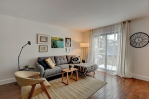 Un salon comprenant un canapé, un fauteuil, une table basse et une lampe. Des tableaux encadrés ornent le mur, et il y a aussi une horloge.