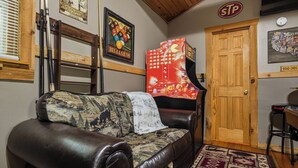 Une pièce avec un canapé en cuir marron, une décoration murale sur le thème du billard, une porte en bois et une horloge murale.