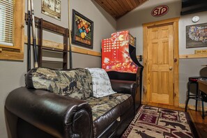 A room with a brown leather sofa, a billiards-themed wall decoration, a wooden door, and a wall clock. - New Listing Hot Tub, Pool Table, Free Attractions (Sevierville)