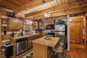 A wooden kitchen with a central island, stainless steel appliances, and a dining area with a chair. - New Listing Hot Tub, Pool Table, Free Attractions (Sevierville)