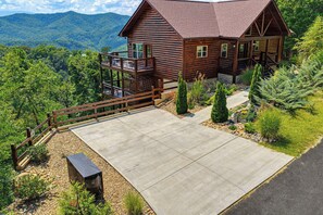 A log cabin with a balcony, surrounded by a well-maintained garden and a view of mountains. - New Listing, Game Room, Hot Tub, Free Attractions, Mountain View (Sevierville)
