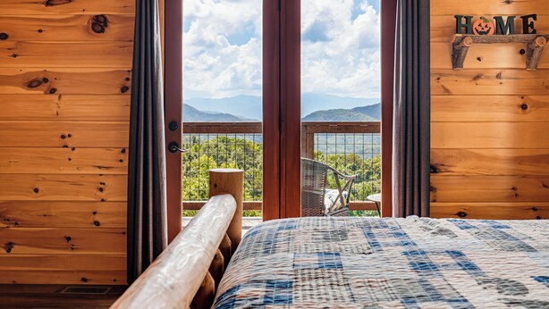 A wooden cabin room with a bed, a window with curtains, and a view of mountains. - New Listing, Game Room, Hot Tub, Free Attractions, Mountain View (Sevierville)