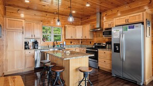 A spacious kitchen with wooden cabinets, a stainless steel refrigerator, a granite countertop, and a central island with stools. - New Listing, Game Room, Hot Tub, Free Attractions, Mountain View (Sevierville)