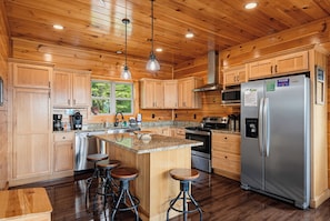A spacious kitchen with wooden cabinets, a stainless steel refrigerator, a granite countertop, and a central island with stools. - New Listing, Game Room, Hot Tub, Free Attractions, Mountain View (Sevierville)
