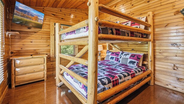 Un letto a castello con un televisore sopra, pareti in legno e un piccolo comò di legno.