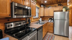 Una cucina con mobili in legno, elettrodomestici in acciaio inossidabile, forno a microonde, forno e frigorifero.