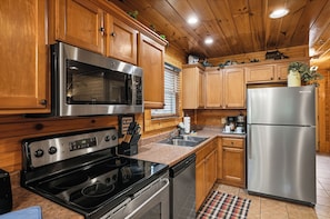 A kitchen with wooden cabinets, stainless steel appliances, a microwave, oven, and a refrigerator. - New Listing | 5BR Gatlinburg Cabin w/ Hot Tub + Game Room + Free Tickets (Gatlinburg)