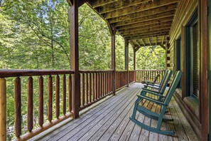 Eine Holzveranda mit Geländer, Schaukelstühlen und Blick auf einen Wald.