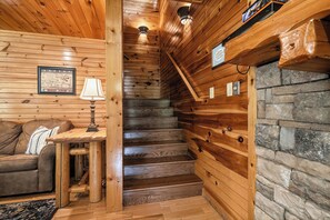 A wooden interior with a staircase, a couch, a lamp, and a framed picture. - New Listing | 5BR Gatlinburg Cabin w/ Hot Tub + Game Room + Free Tickets (Gatlinburg)