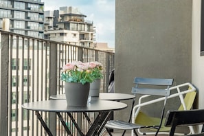 En balkon med et rundt bord, en potteplante med lyserøde blomster og en metalstol.