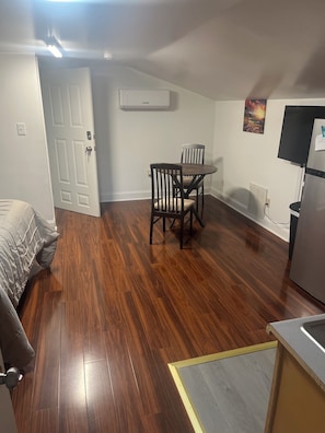 A room with a dining table and chairs, a door, a radiator, and a refrigerator.