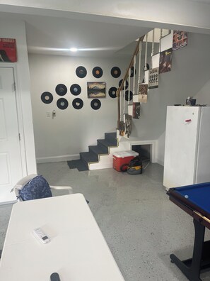 A room with a pool table, a staircase, and a wall decorated with vinyl records.