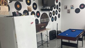 A room with a pool table, a refrigerator, and a wall decorated with vinyl records.