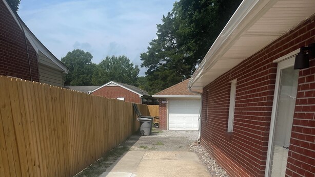 A residential driveway with a wooden fence, a concrete path, and a garage door.