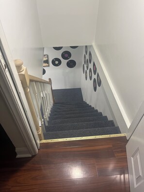 Una escalera con barandilla de madera, escalones alfombrados y una pared decorada con discos de vinilo.