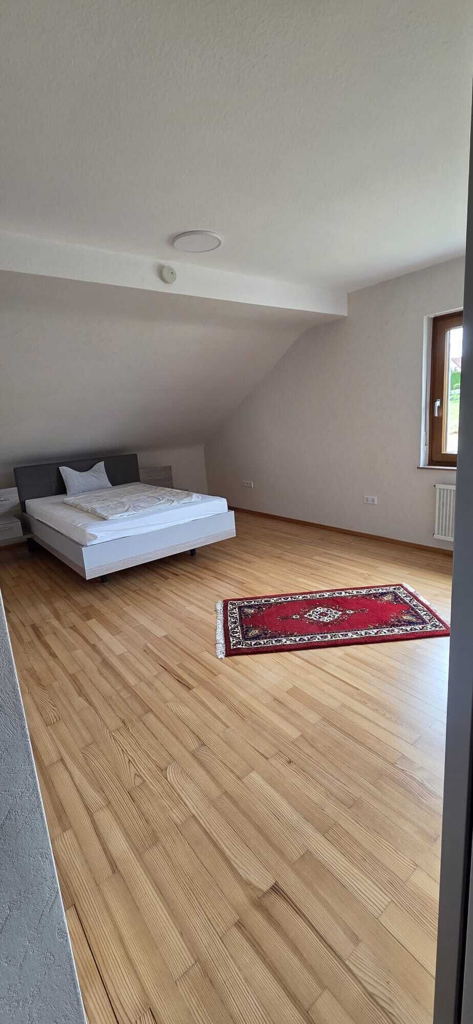 A bedroom with a bed, a red patterned rug, and a sloped ceiling.