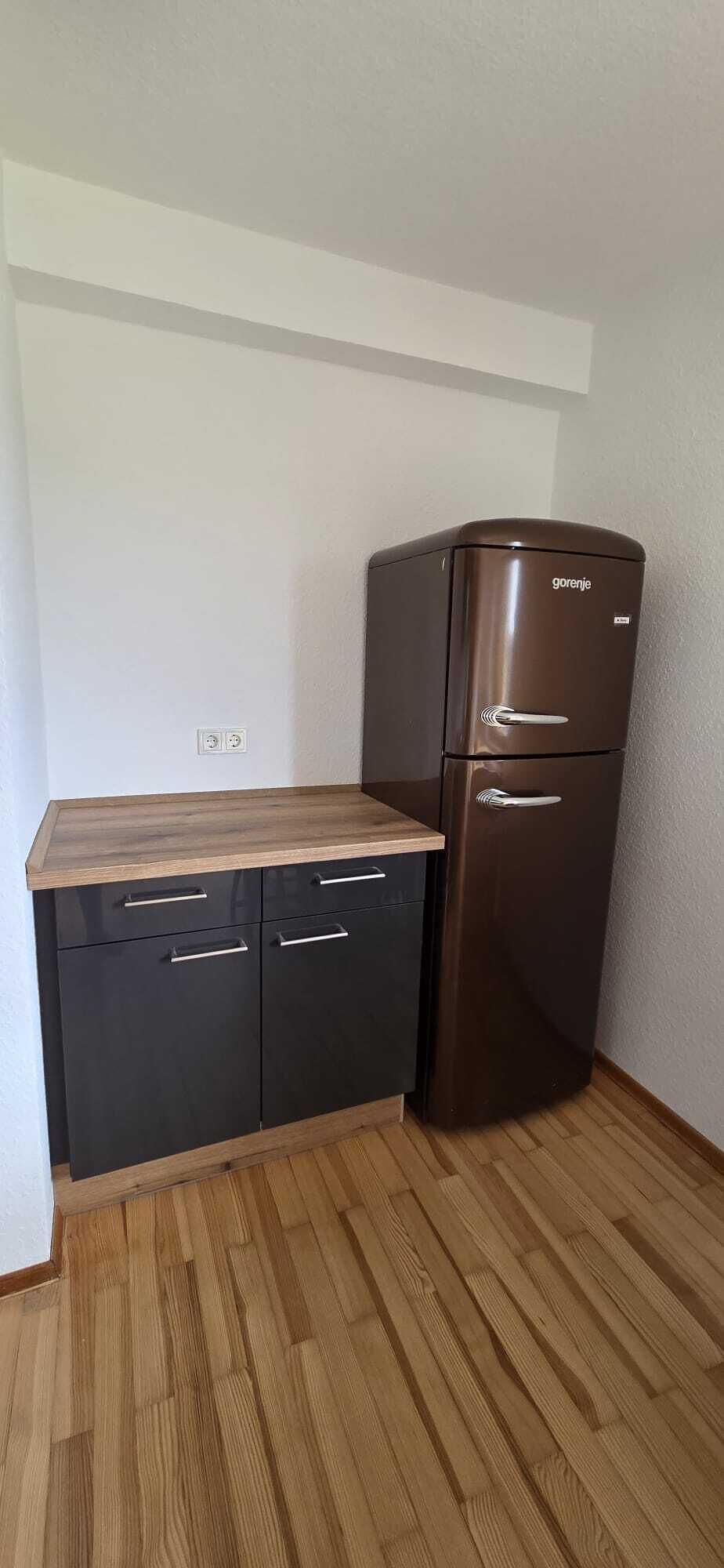 Eine Küchenzeile mit Holzarbeitsplatte, schwarzen Schränken und einem Edelstahlkühlschrank.