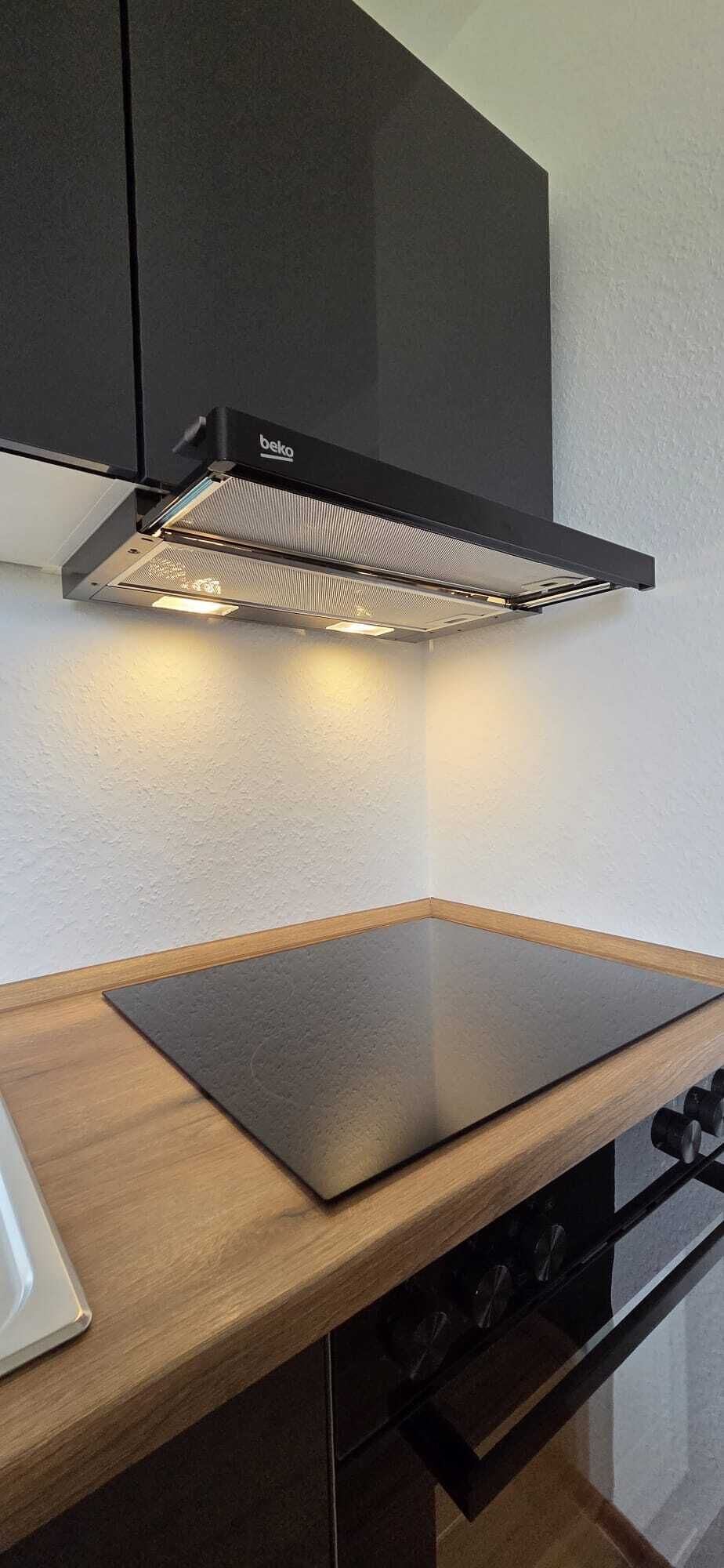 A kitchen with a black range hood, a wooden countertop, and a stove.