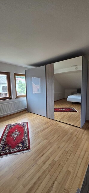 A room with a wooden floor, a red rug, and a bed in the background. - Cozy Vacation Rental "Haus Anna" in the Beautiful Hochwald (Baldringen)