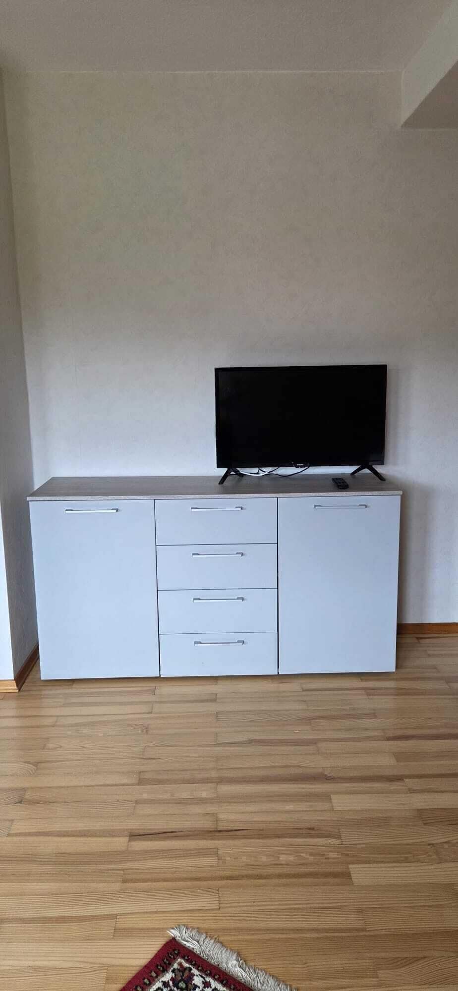 A white cabinet with a flat-screen TV on top, drawers, and a remote control on the cabinet's surface.