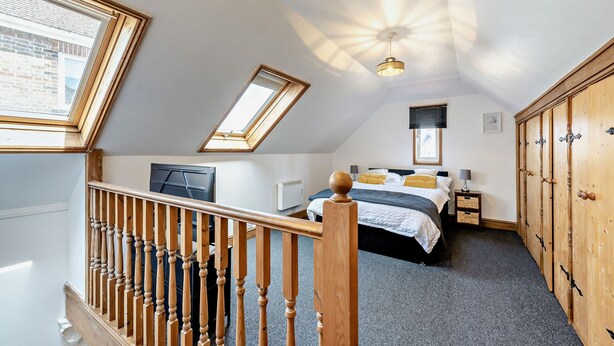 Ein Schlafzimmer mit schrägem Dach, einem Bett, einem Schreibtisch, einem Stuhl, einem Kleiderschrank und einer Treppe.