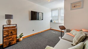 Ein modernes Wohnzimmer mit Flachbildfernseher, einer Holzkommode, einem grauen Sofa und einem kleinen Tisch.