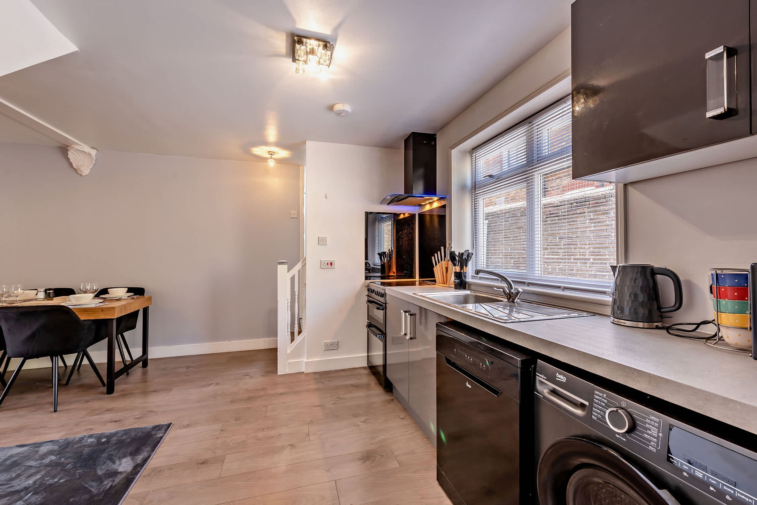 A modern kitchen with a dishwasher, a coffee maker, and a window with blinds.