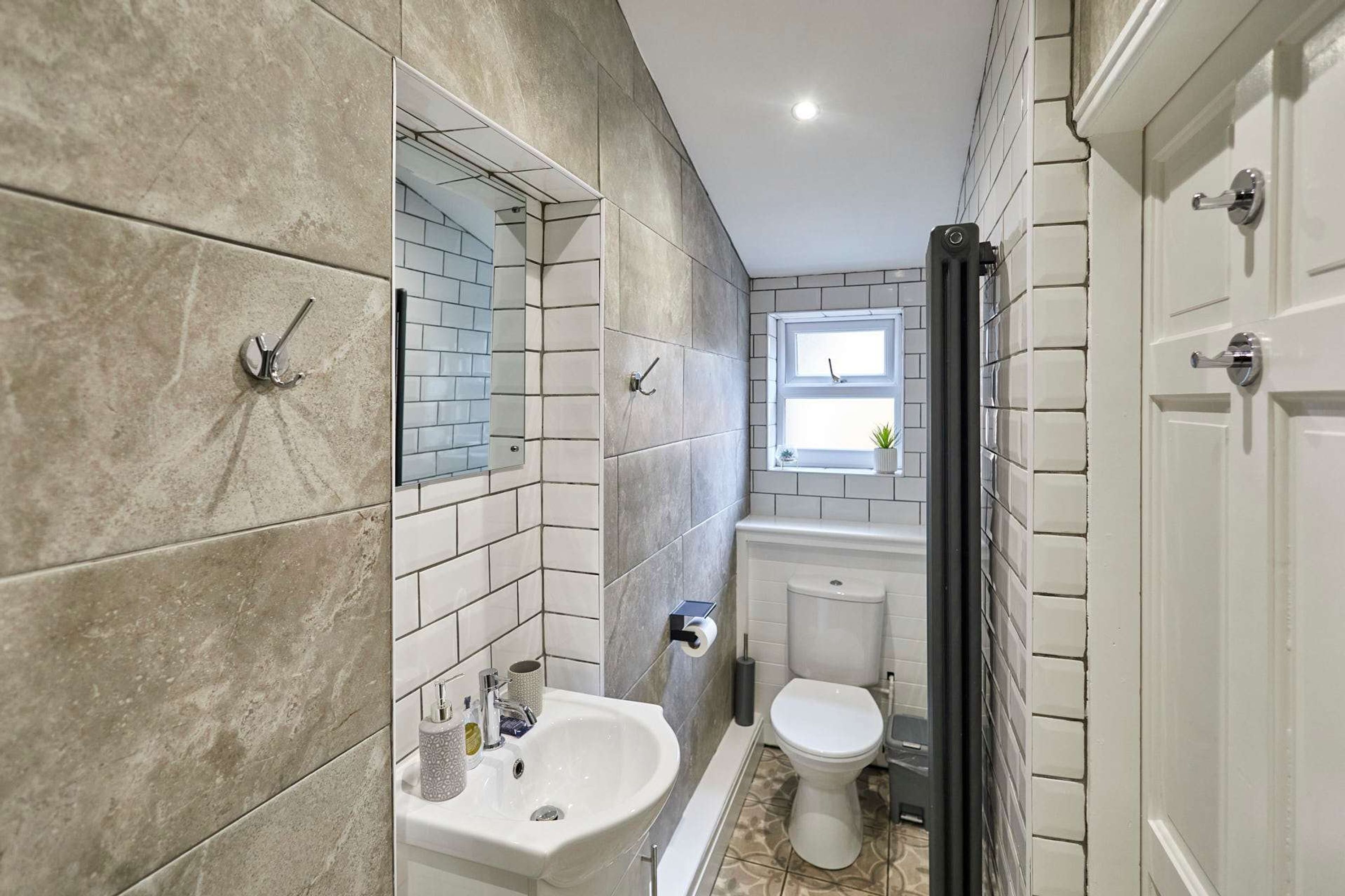 A bathroom with a white sink, a toilet, and a mirror. There is a window above the toilet.