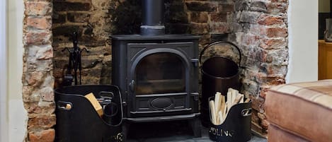 A wood-burning stove with a chimney, a black pot with a handle, and a basket filled with logs.