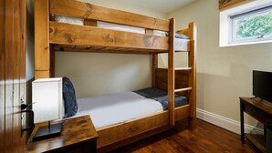A bunk bed with a desk and a television in a room with wooden flooring and a window. - Host Stay - Hidden Winds Cottage (Guisborough)