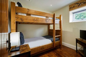 Ein Stockbett mit Schreibtisch und Fernseher in einem Zimmer mit Holzboden und Fenster.