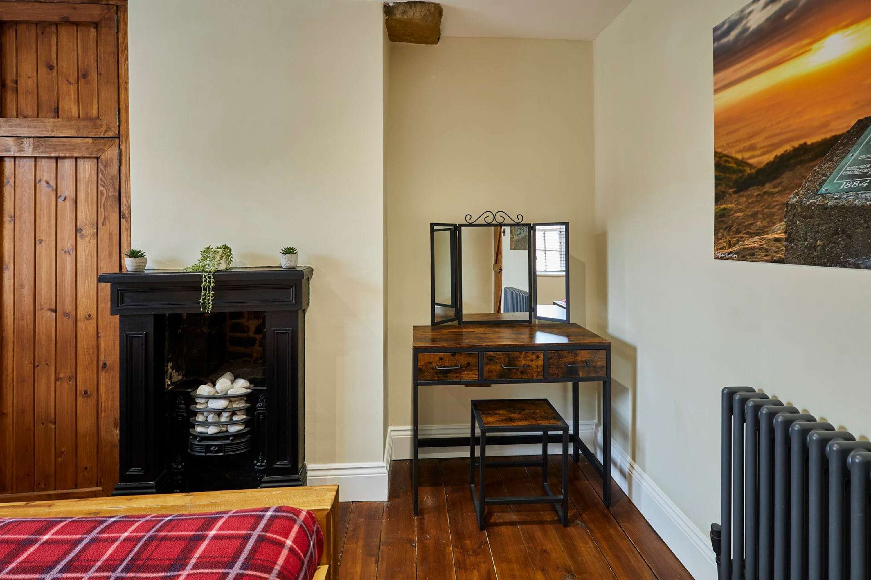 A room with a fireplace, a wooden desk, a mirror, a radiator, and a painting on the wall.