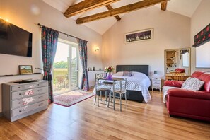 A bedroom with a bed, a red sofa, a desk with a chair, a dresser, a TV, and a window with curtains. - Host Stay Snowy Owl Barn (Thetford)