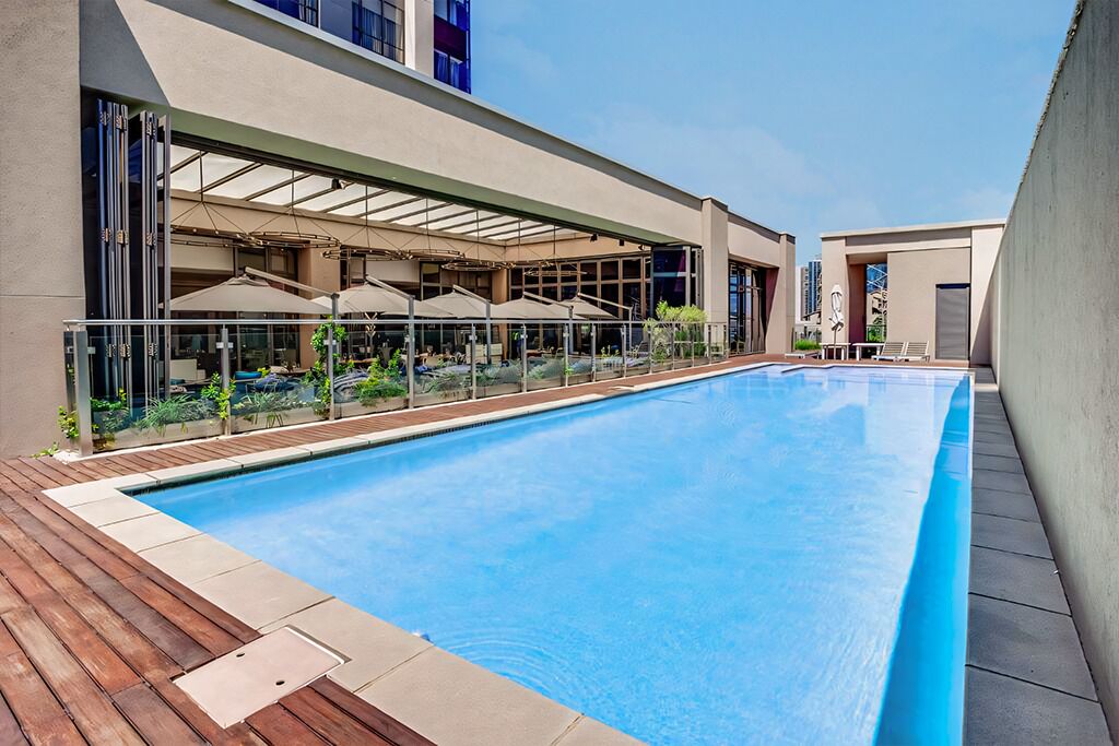 A swimming pool with a wooden deck, glass balustrades, and umbrellas.