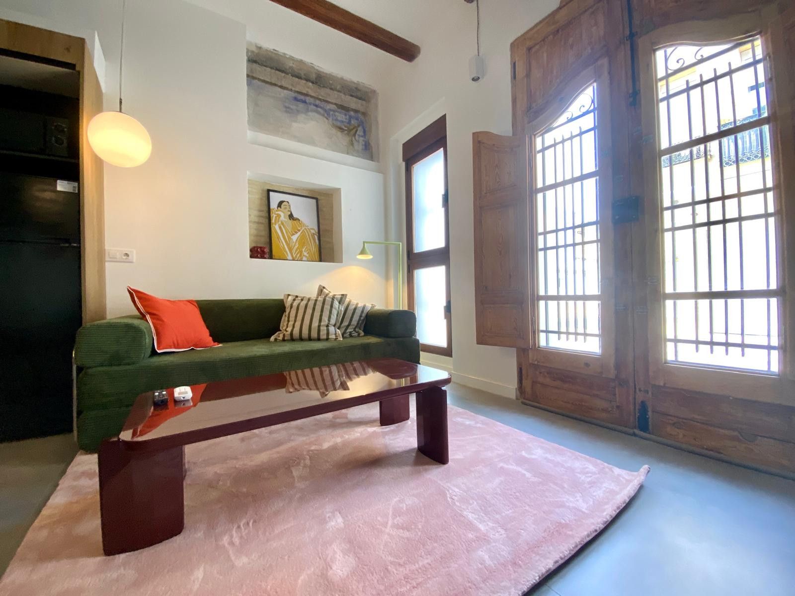 A living room with a green sofa, a wooden coffee table, and a large window with bars.