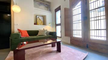 A living room with a green sofa, a wooden coffee table, and a large window with bars.
