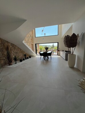 A spacious interior with a stone wall, a dining area with a table and chairs, and a large window. - Luxury Villa for Rent (Salernes)