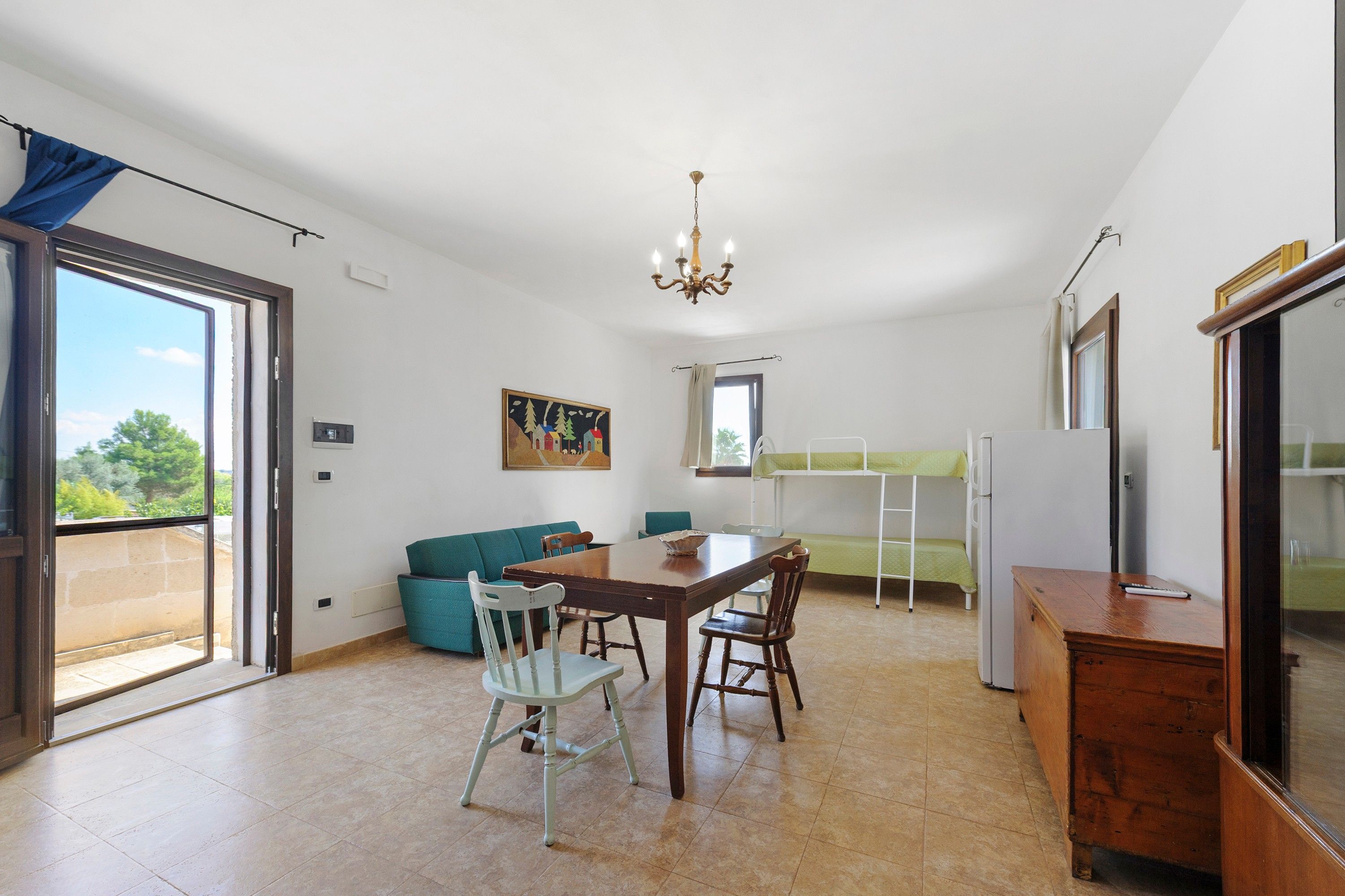 Una habitación amplia con una mesa de comedor, sillas, un sofá, una cama nido y una araña.