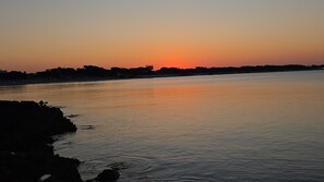 Un fiume tranquillo al tramonto, con la sagoma di edifici sull'altra sponda.