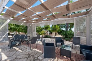 Un'area relax esterna coperta, con mobili in vimini e una struttura a pergola.