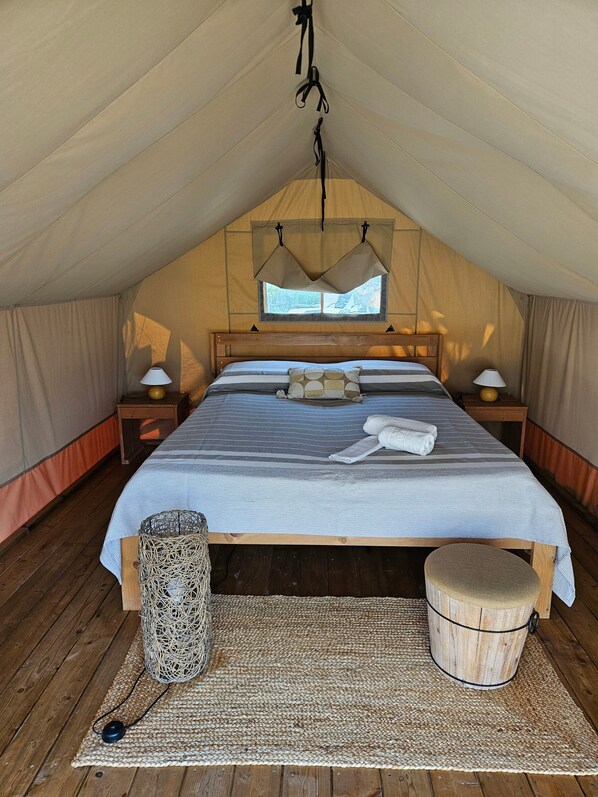 A tented room with a bed, bedside lamps, a woven basket, and a small stool.