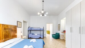 Een hotelkamer met een stapelbed, een houten garderobe, een bureau met lamp en een groene fauteuil.