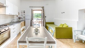Een compacte keuken met een eettafel en stoelen, een kleine zithoek en uitzicht op een terras.