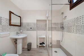 A bathroom with a sink, mirror, shower, and a small shelf with toiletries. - Fico d'India Room (Porto Cesareo)