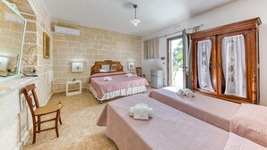 Une chambre avec deux lits, une chaise en bois, une petite table et une armoire avec des rideaux en dentelle.